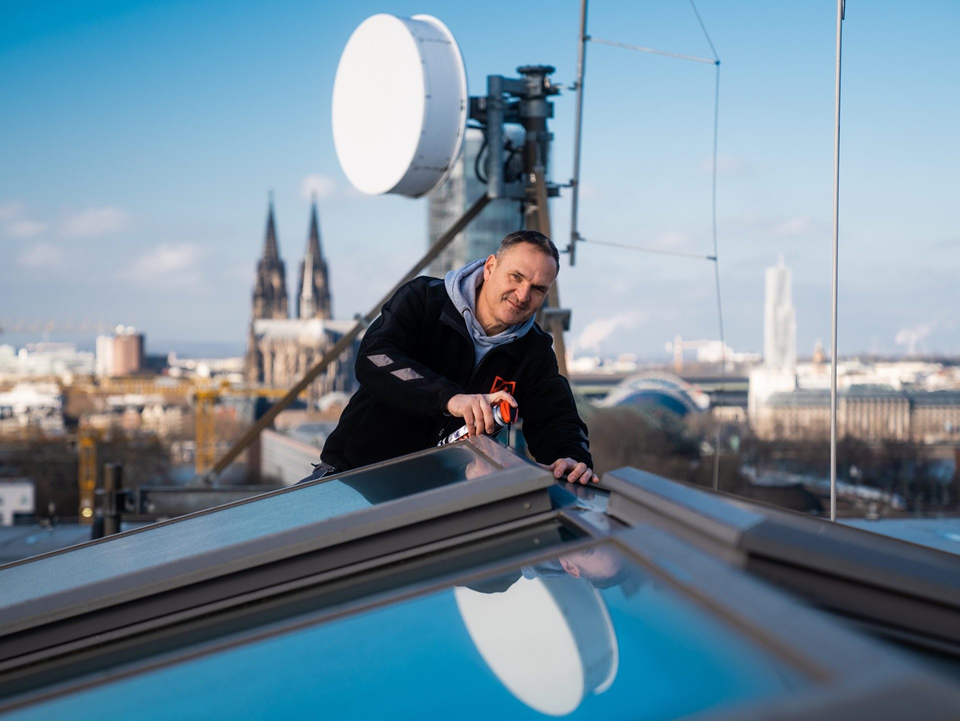 Techniker montiert Anlage auf einem Dach über der Kölner Skyline